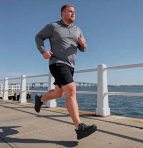 A man in athletic wear jogging along a scenic boardwalk wearing black Propét Men's B10 Usher sneakers.