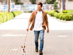 A man smiling while walking his small dog on a paved path, wearing supportive sneakers that provide stability and balance.