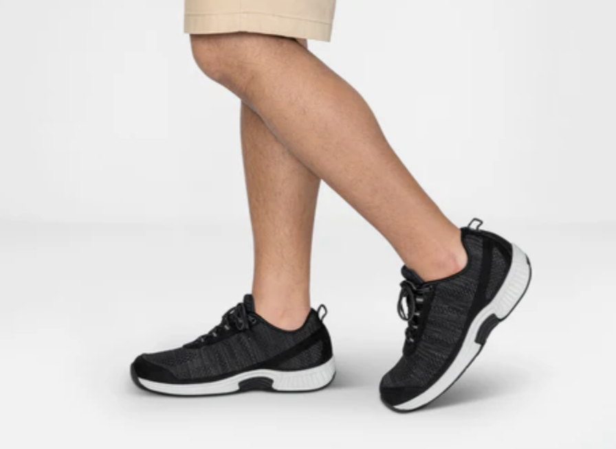 Pair of black knitted running shoes with a white sole, shown in mid-stride.