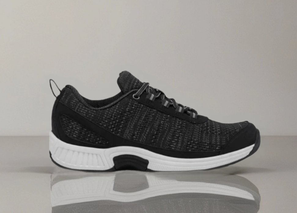 Black knit sneaker with a white sole on a reflective surface.