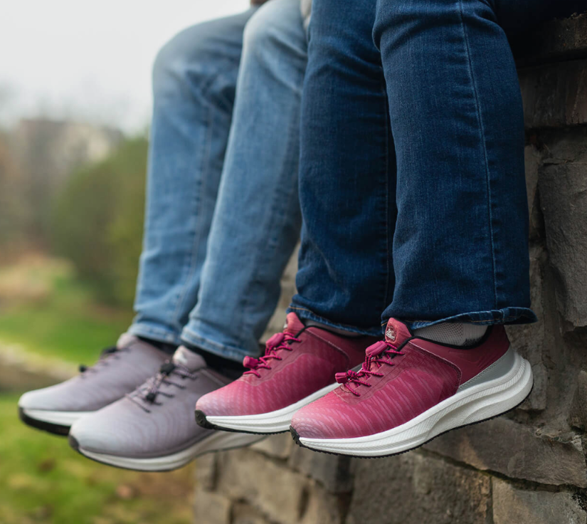 Three people sit on a stone ledge wearing jeans and colorful athletic sneakers (pink, purple, blue).