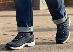 Person wearing dark gray knit sneakers with a white sole and rolled cuffs, walking on concrete pavement.