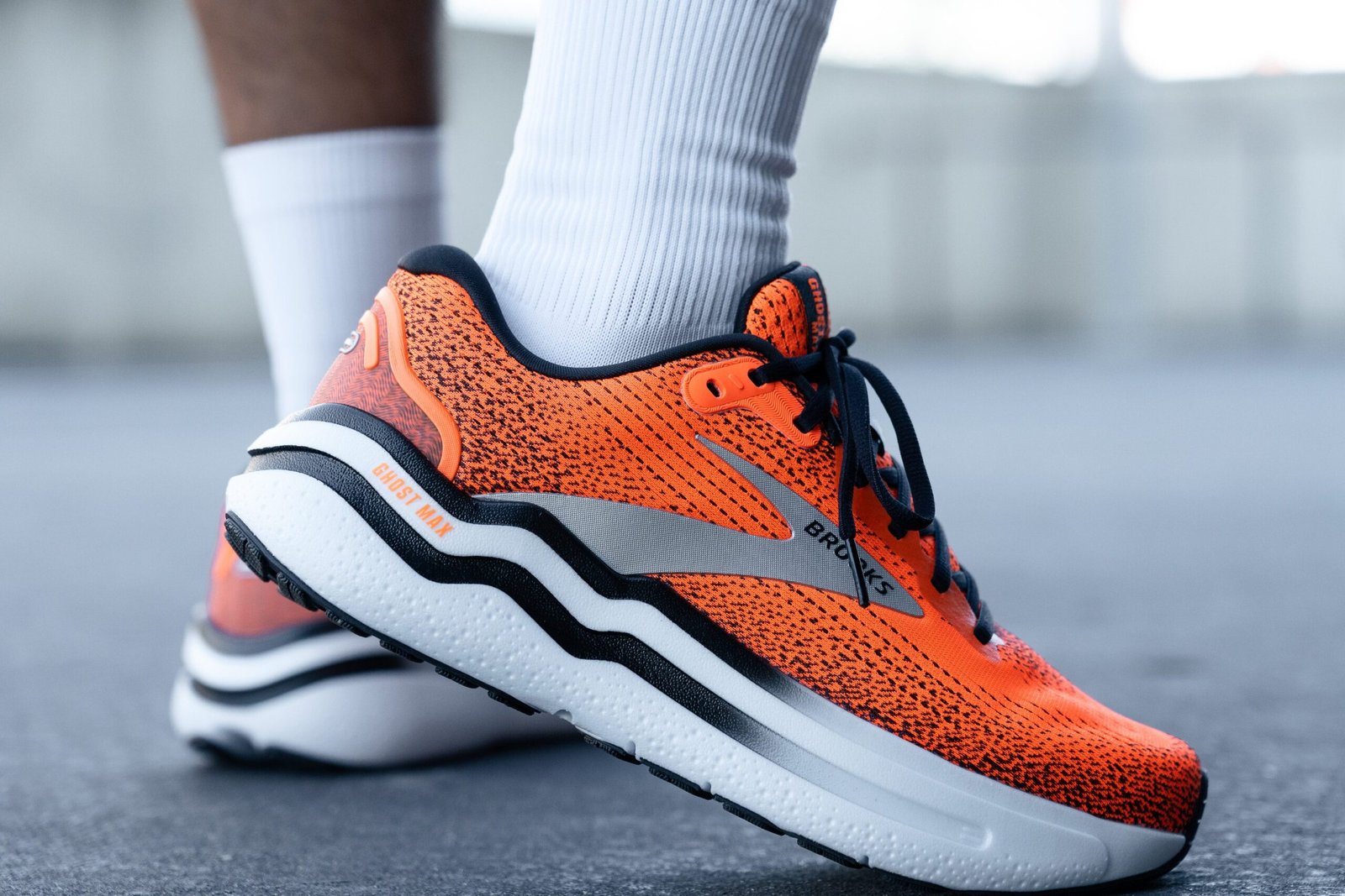 Close-up of bright orange running shoe with black speckled pattern and white midsole on pavement.
